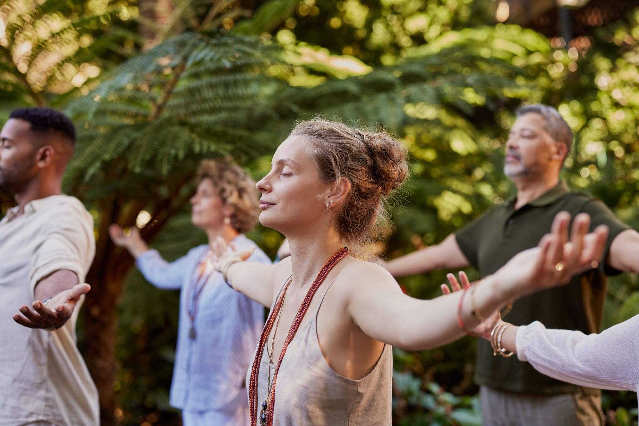 People meditating outdoors with arms outstretched.
