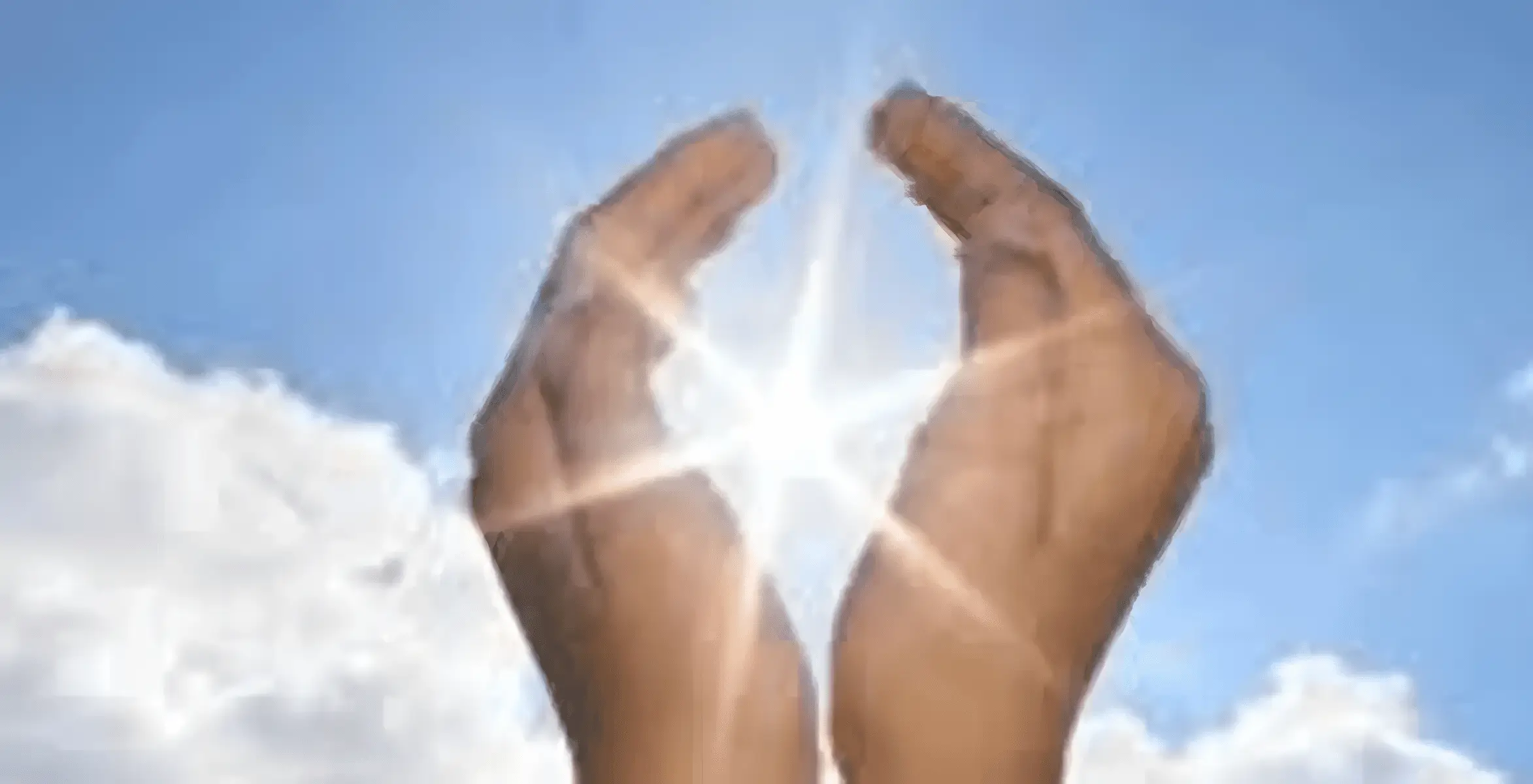 Hands framing bright sunlight against a blue sky.